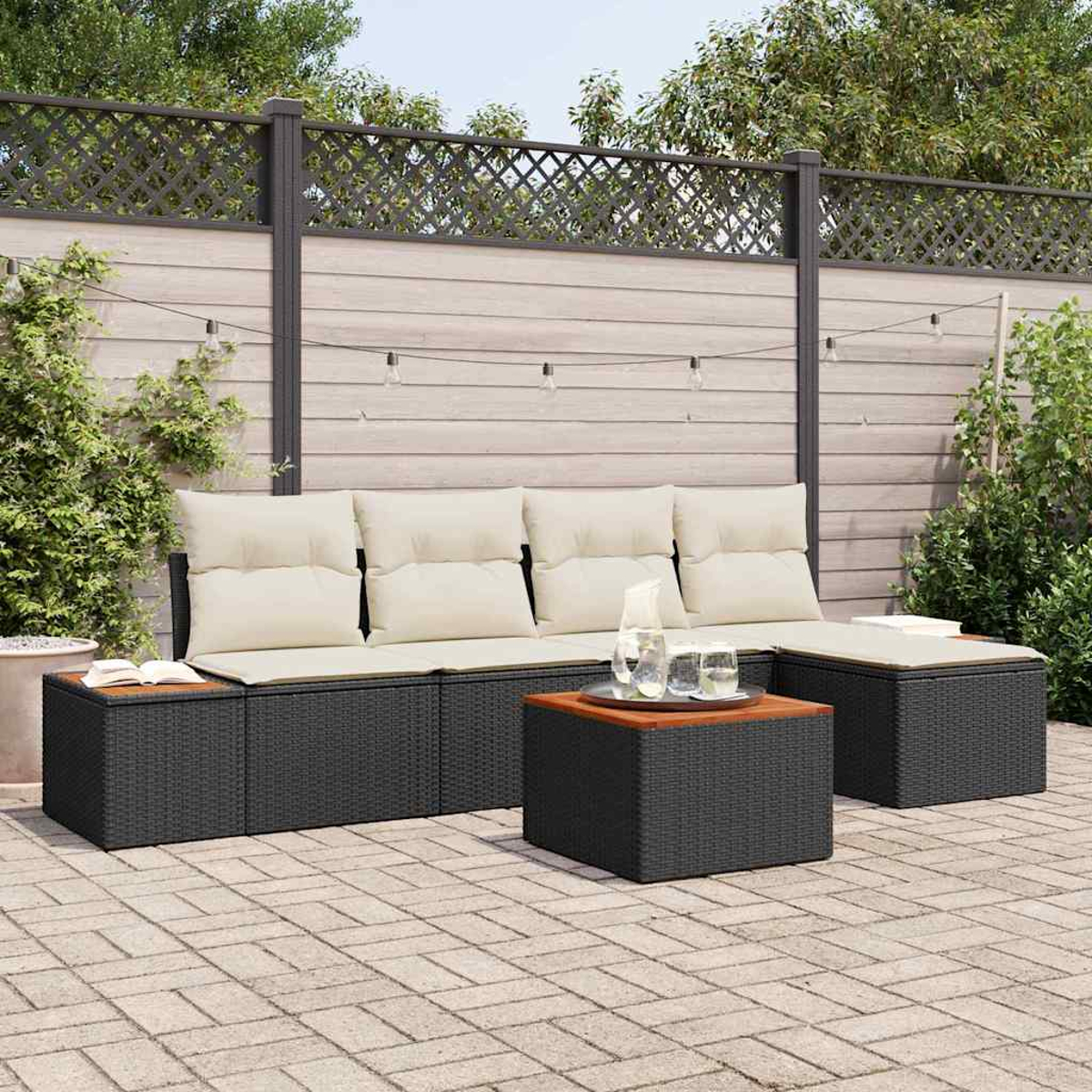 Garten-Sitzgruppe mit cremefarbenen Kissen, schwarzen gewebten Unterbauten. Mit Tisch mit Holzplatte. Hintergrund: Terrasse, Zaun, Grün.