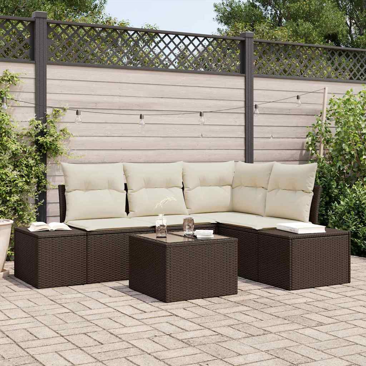 Juego de patio al aire libre con muebles de mimbre marrón y cojines crema. Una mesa pequeña al frente. Una valla de madera en el fondo.