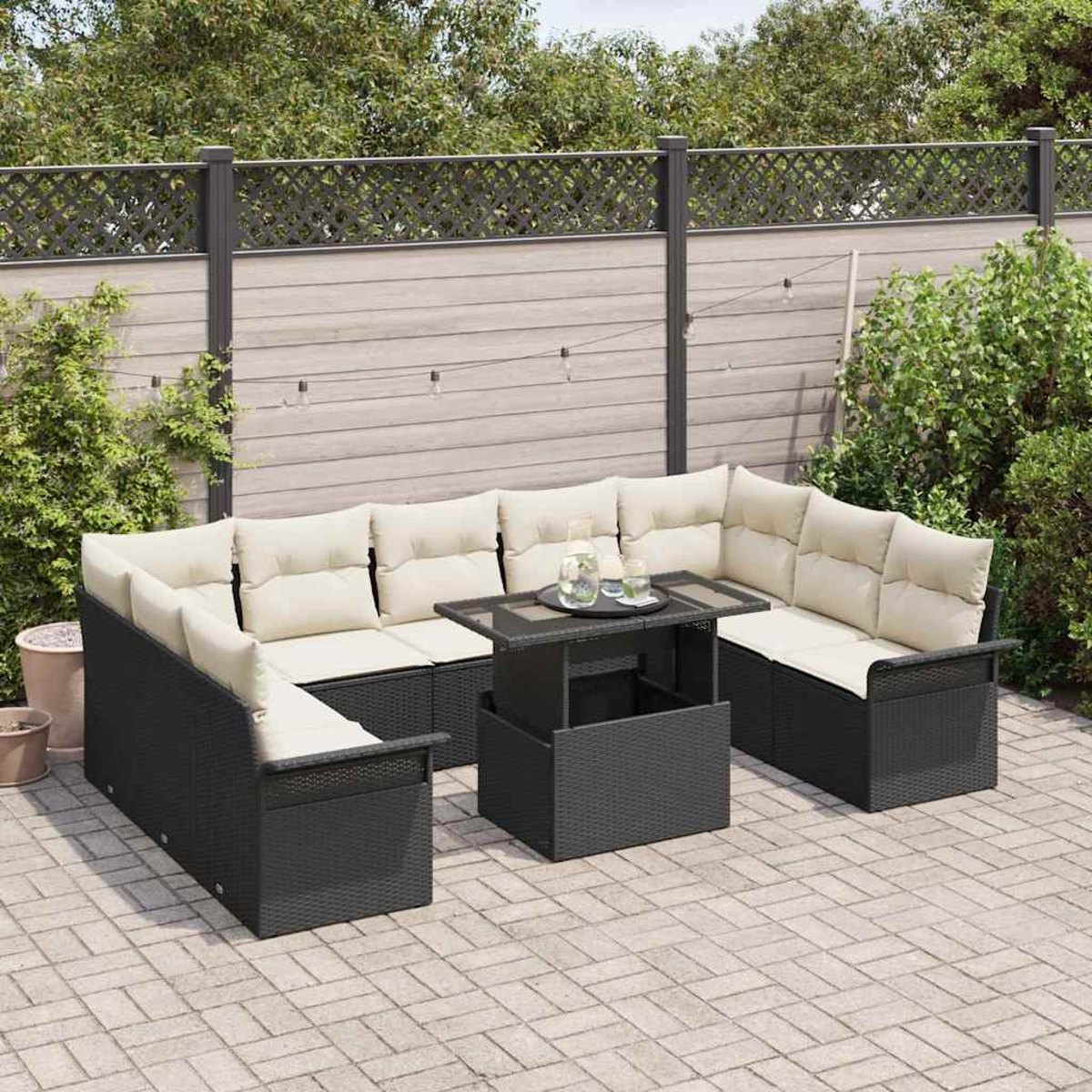 Garten-Terrassenset mit schwarzen Korbsesseln, cremefarbenen Kissen und einem Tisch mit Getränken. Holzzaun und Grün in Hintergrund.