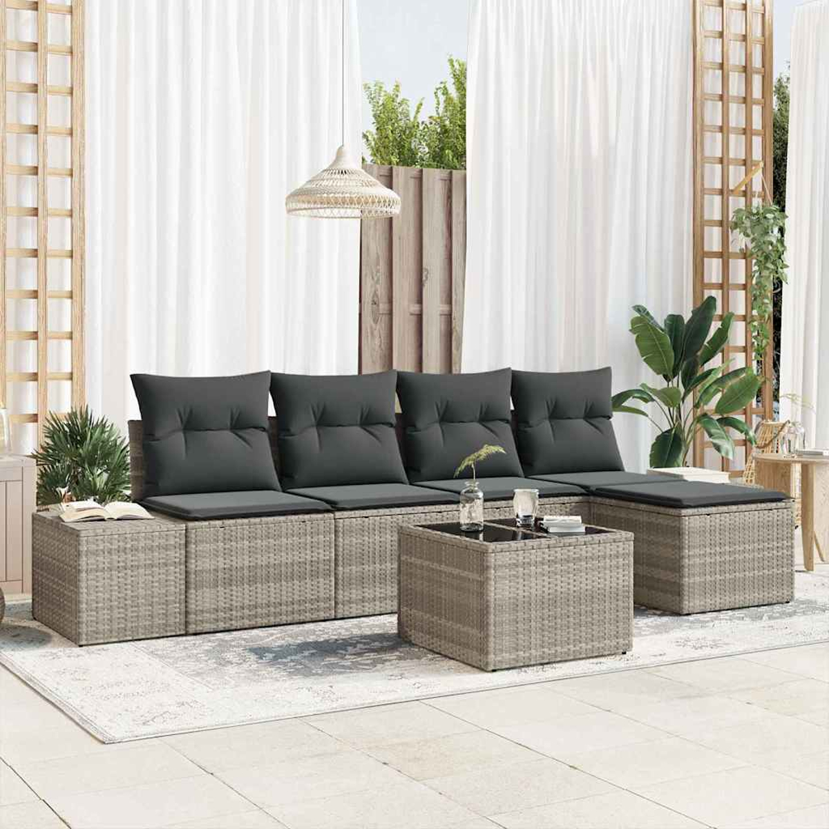 Außenbereich mit grauem Korbsessel, Kissen und Couchtisch. Weiße Vorhänge und Pflanzen im Hintergrund.