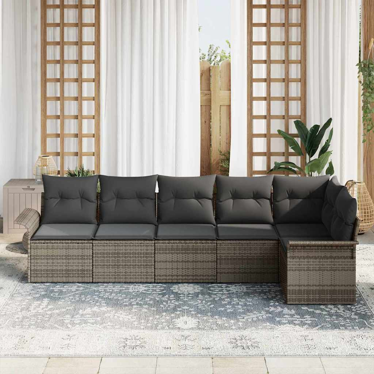 Ein Ecksofa im Freien mit grauen Kissen steht auf einem Teppich. Dahinter befinden sich weiße Vorhänge, Holzgitter und eine Pflanze.