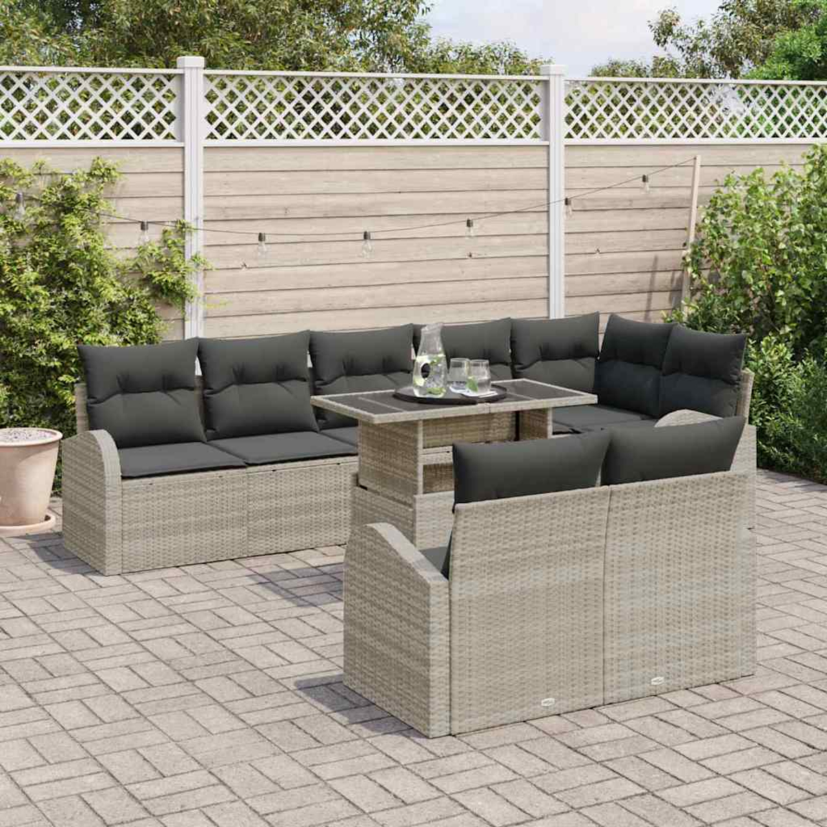 Garten-Sitzgruppe mit grauen Kissen und einem Tisch. Im Hintergrund befinden sich ein Zaun, Grün und eine Ziegelterrasse.