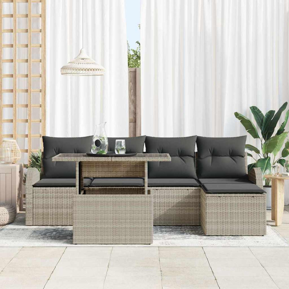Gartenmöbel-Set mit grau gepolstertem Sofa, Tisch und weißen Vorhängen. Im Hintergrund eine Pflanze. Die Möbel sind aus Rattan.