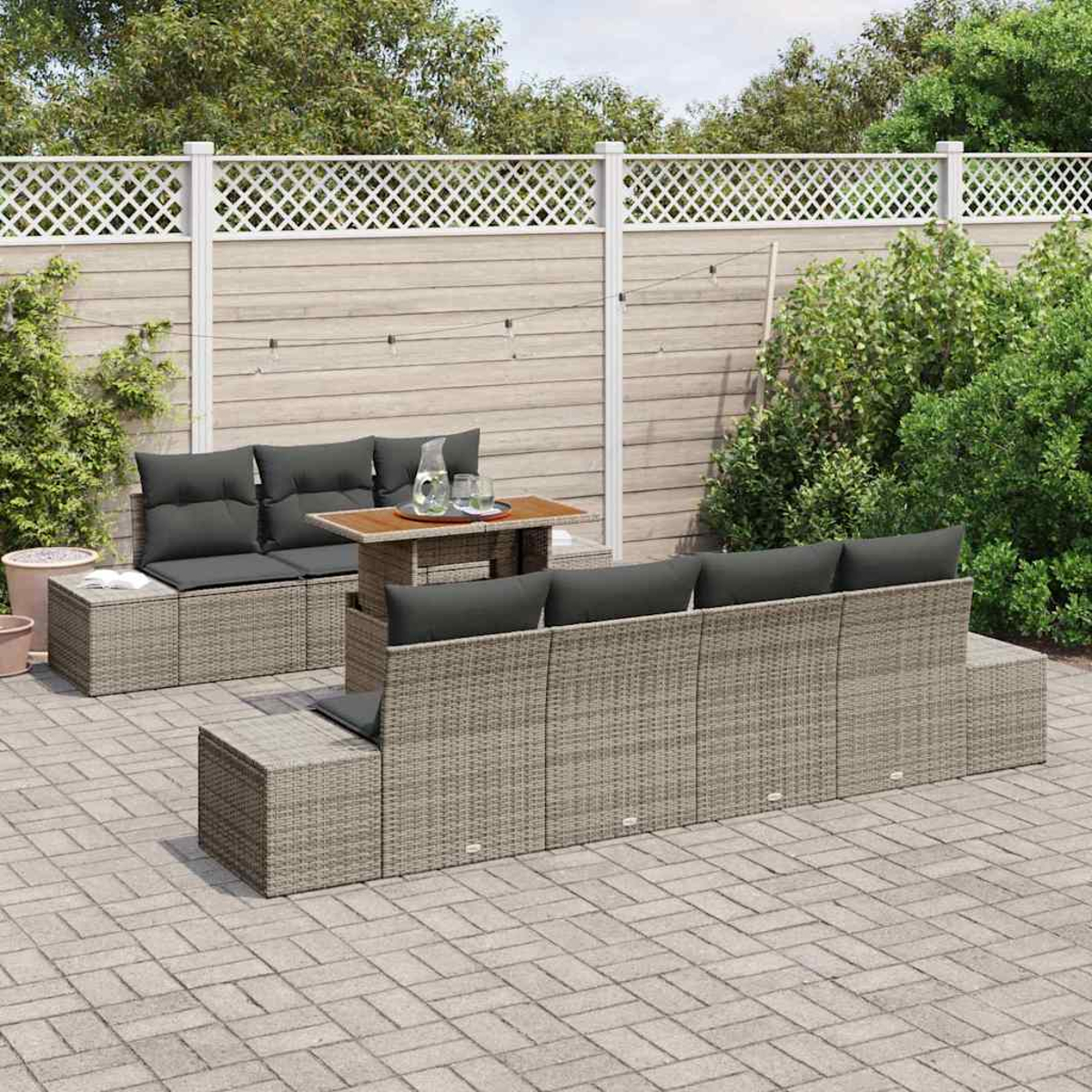 Garten-Sitzgruppe mit grauen Kissen und einem Tisch. Hintergrund: Holzzaun, Grün und gepflasterte Terrasse.