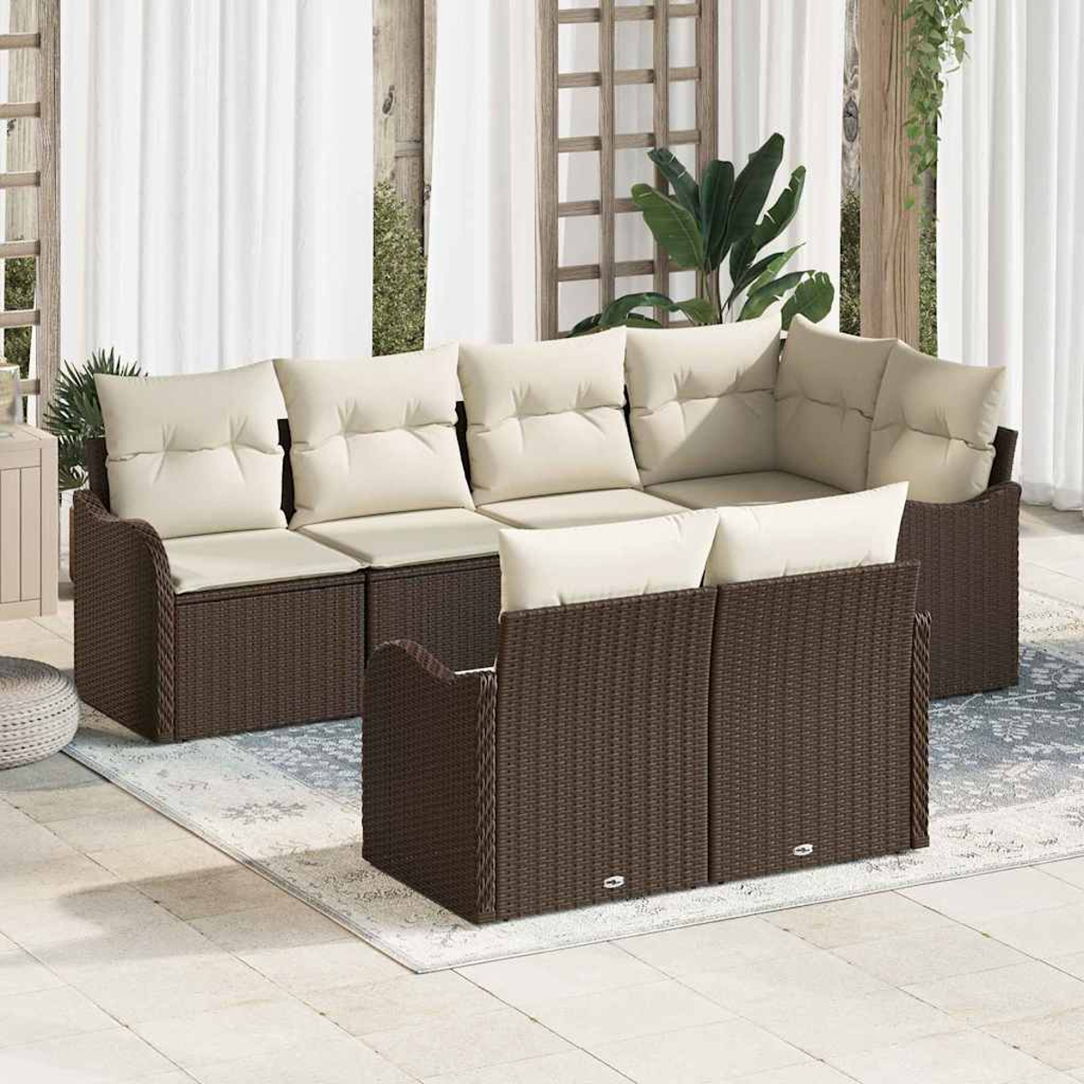 Braunes Outdoor-Korbsessel-Set mit cremefarbenen Kissen. Weiße Vorhänge und Pflanzen im Hintergrund. Auf einem gemusterten Teppich.