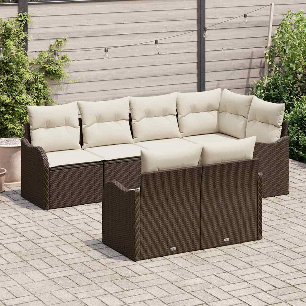 Braunes Wicker-Ecksofa für den Außenbereich mit cremefarbenen Kissen auf einer Steinterrasse. Der Hintergrund umfasst einen Holzzaun und Grün.