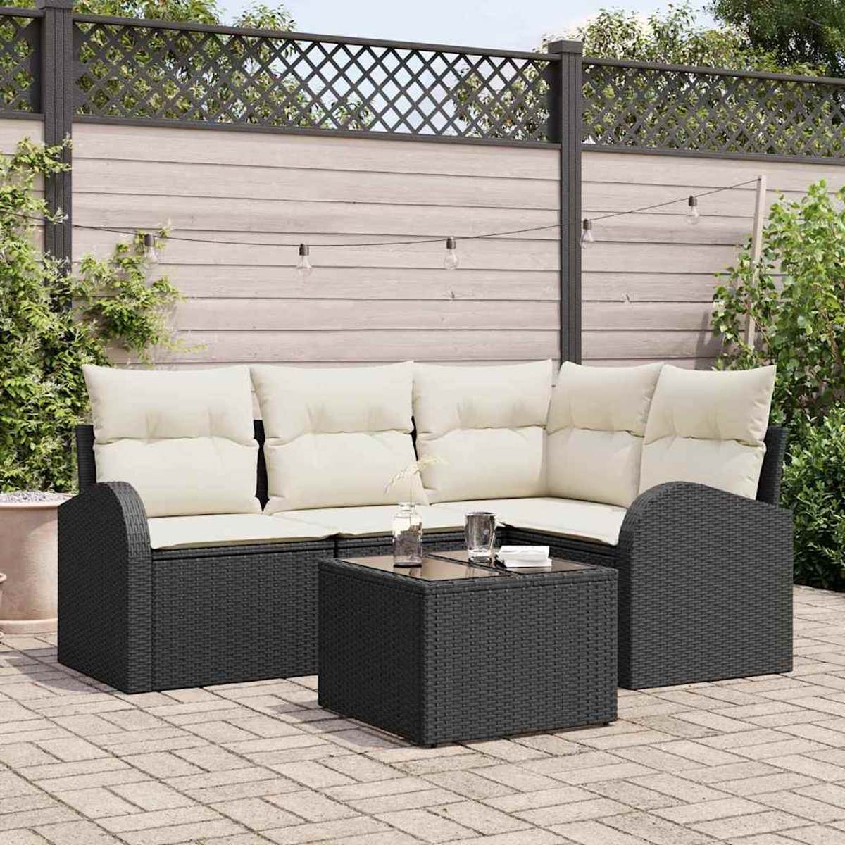 Juego de patio exterior: sofá negro tejido con cojines crema, mesa a juego y valla de madera con luces.