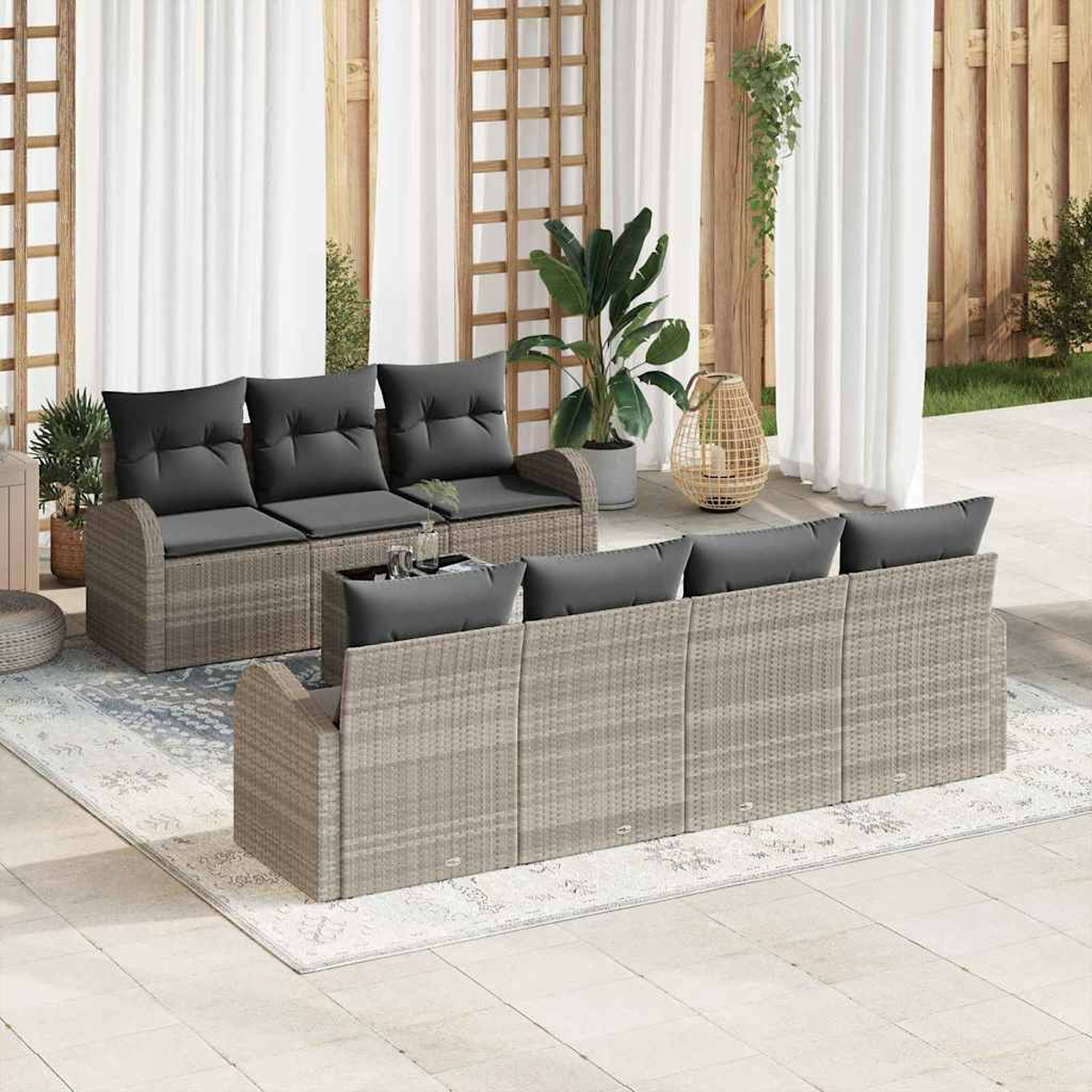 Garten-Sitzgruppe mit grauen Kissen auf einem Teppich. Pflanzen und Vorhänge im Hintergrund. Szene ist auf einer Terrasse.