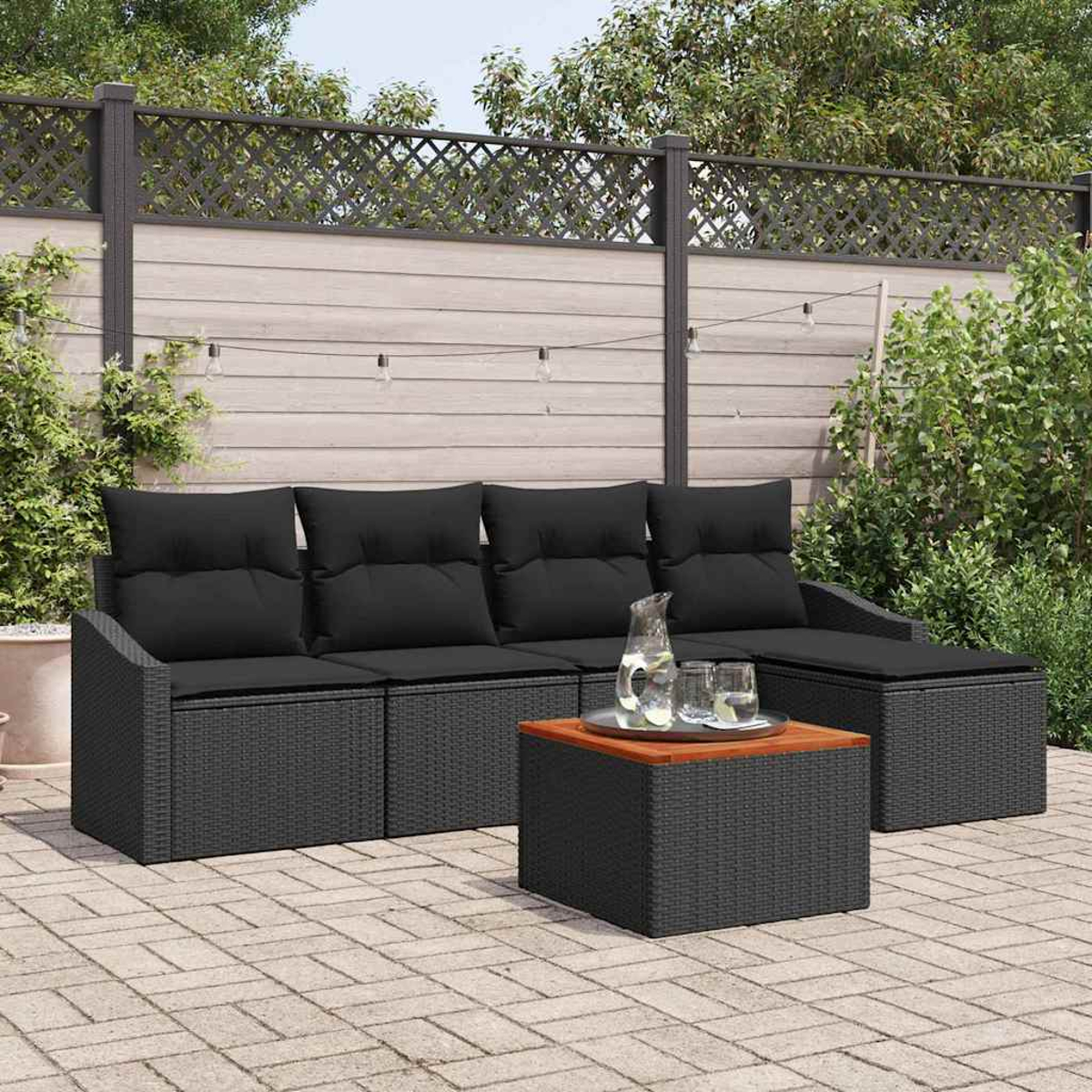 Garten-Terrassenset mit schwarzen Kissen, Tisch und Getränken. Auf einer Backstein-Terrasse mit Holzzaun und Grün im Hintergrund.