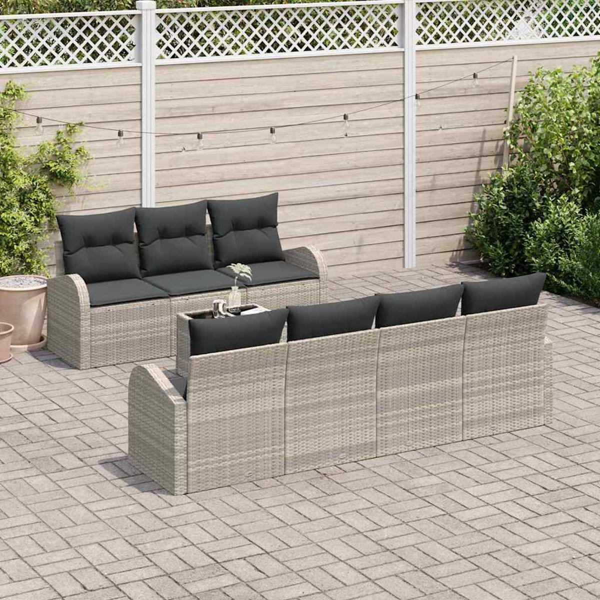 Garten-Terrassenset mit grauen Kissen. Korbmöbel auf einer Backsteinterrasse, einem weißen Zaun und Grün im Hintergrund.