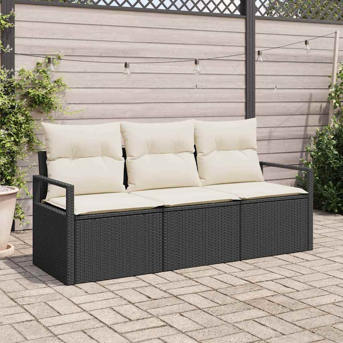 Ein dunkelgraues Rattansofa mit cremefarbenen Kissen steht auf einer Ziegelterrasse. Der Hintergrund umfasst einen Holzzaun und Hängelampen.