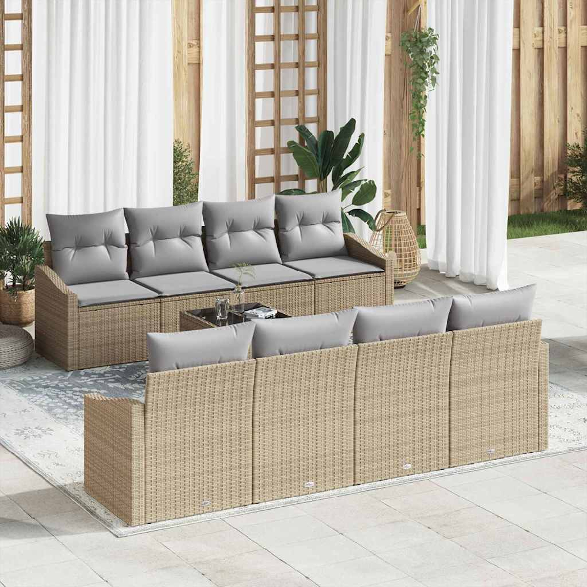 Garten-Sitzgruppe mit hellbraunen Korbs Sofas und grauen Kissen. Weiße Vorhänge und Holzgitter im Hintergrund, Pflanzen an den Seiten.