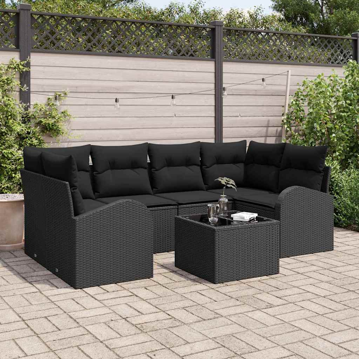 Ein schwarzes Outdoor-Sofa aus Korbgeflecht mit schwarzen Kissen und einem schwarzen quadratischen Tisch auf einer Terrasse.