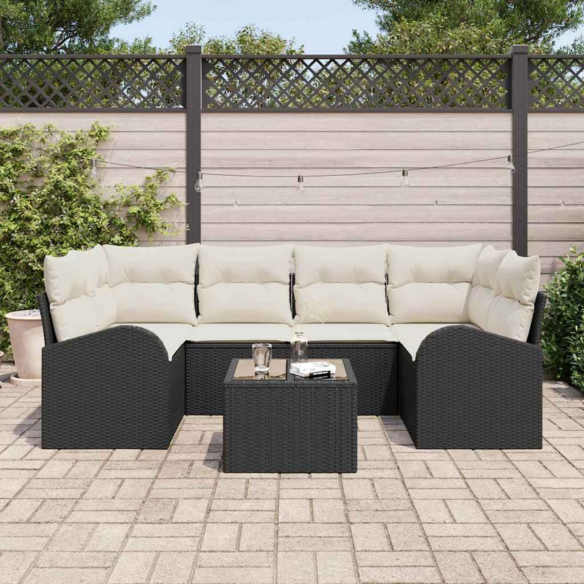 Outdoor-Ecksofa mit cremefarbenen Kissen und einem kleinen quadratischen Tisch. Auf einer Terrasse. Holzzaun und Grün im Hintergrund.