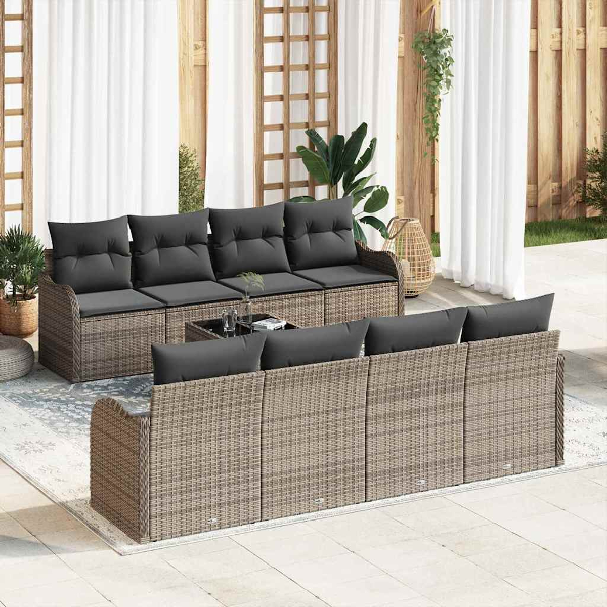 Garten-Sofa-Set mit Korbmöbeln und grauen Kissen. Beinhaltet zwei Sofas, einen Tisch und Pflanzen, vor weißen Vorhängen.
