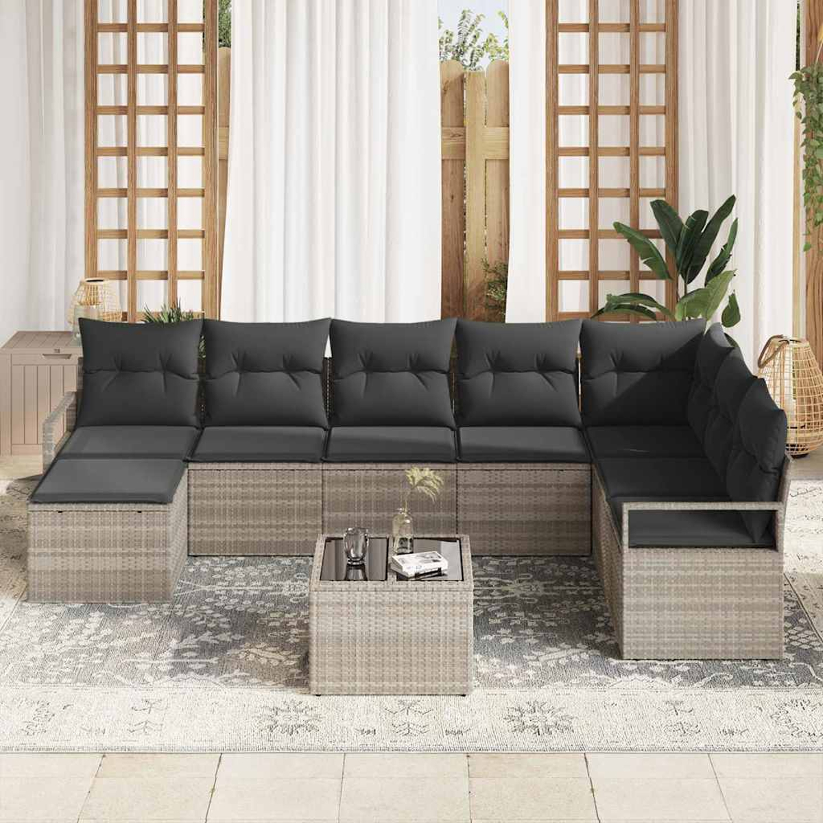 Ein Ecksofa im Freien mit grauen Kissen, einem kleinen Tisch und einem gemusterten Teppich. Der Hintergrund zeigt ein Fenster und Pflanzen.