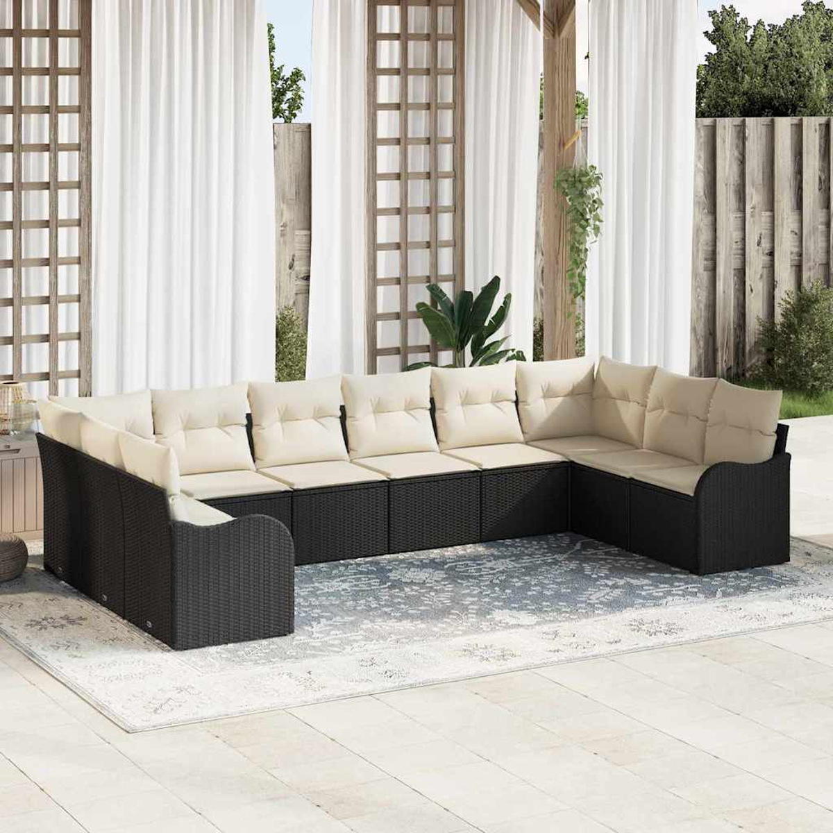 Sofá seccional exterior con cojines beige sobre una alfombra estampada, cortinas al fondo. Marco de mimbre negro.