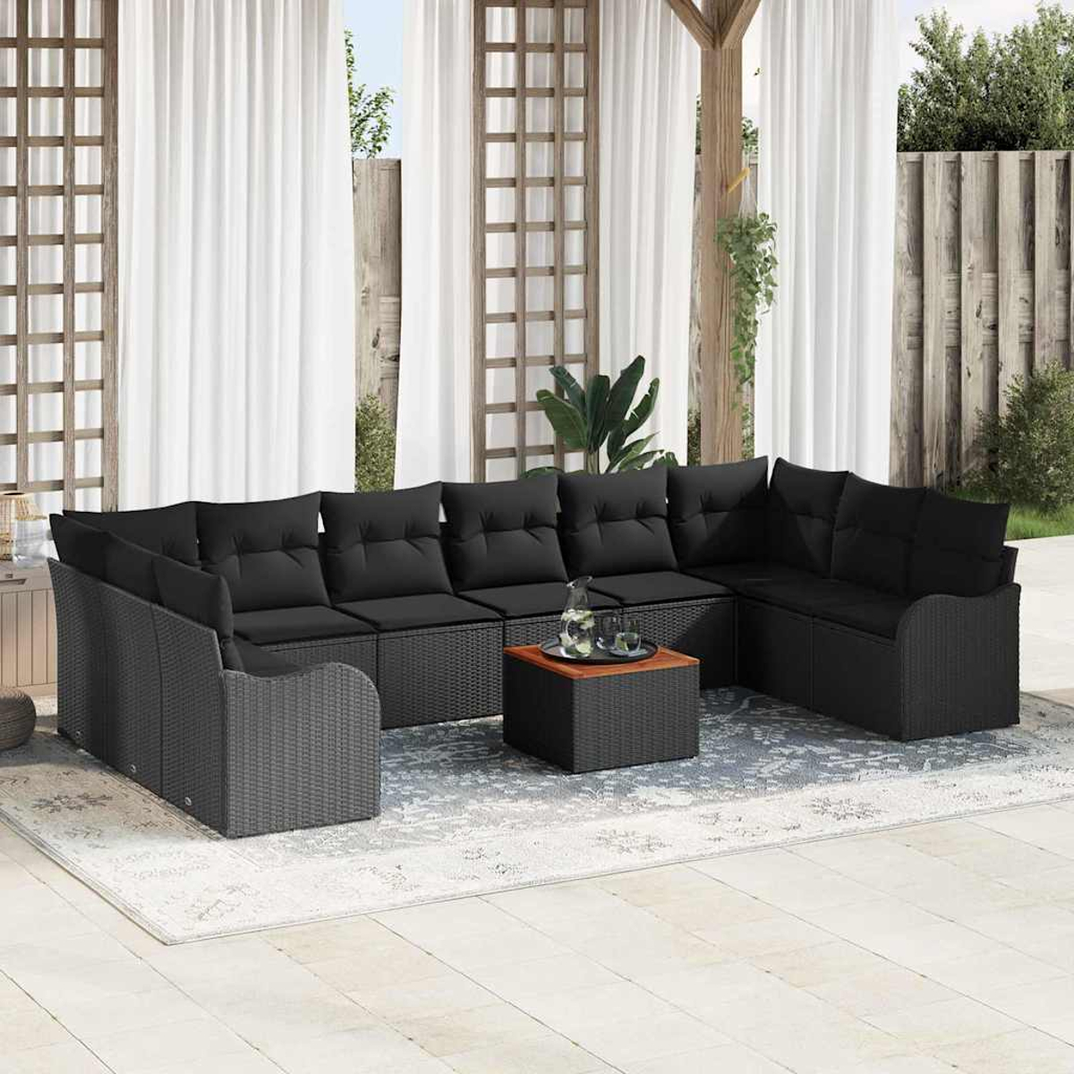 Outdoor-Ecksofa mit schwarzen Kissen, Couchtisch mit Getränken und weißen Vorhängen im Hintergrund.