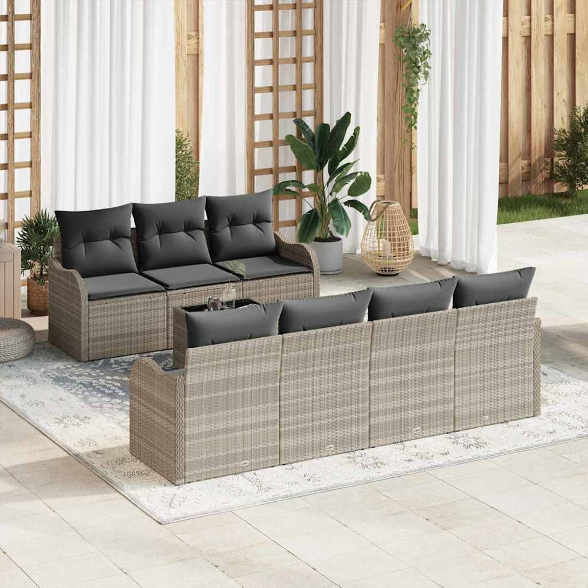 Szene im Freien mit Rattansofas, grauen Kissen, Pflanzen und einem Teppich. Weiße Vorhänge und Holzgitter im Hintergrund.
