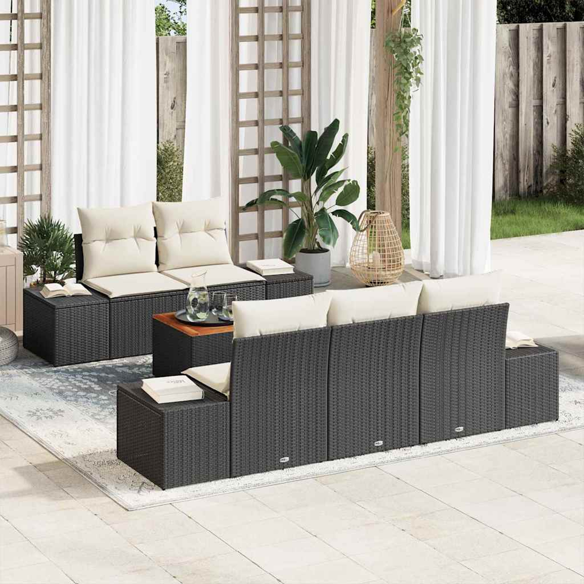 Gartenmöbel-Set mit schwarzer Korbmöbel, beigen Kissen, kleinen Tischen, Pflanzen und weißen Vorhängen im Hintergrund.