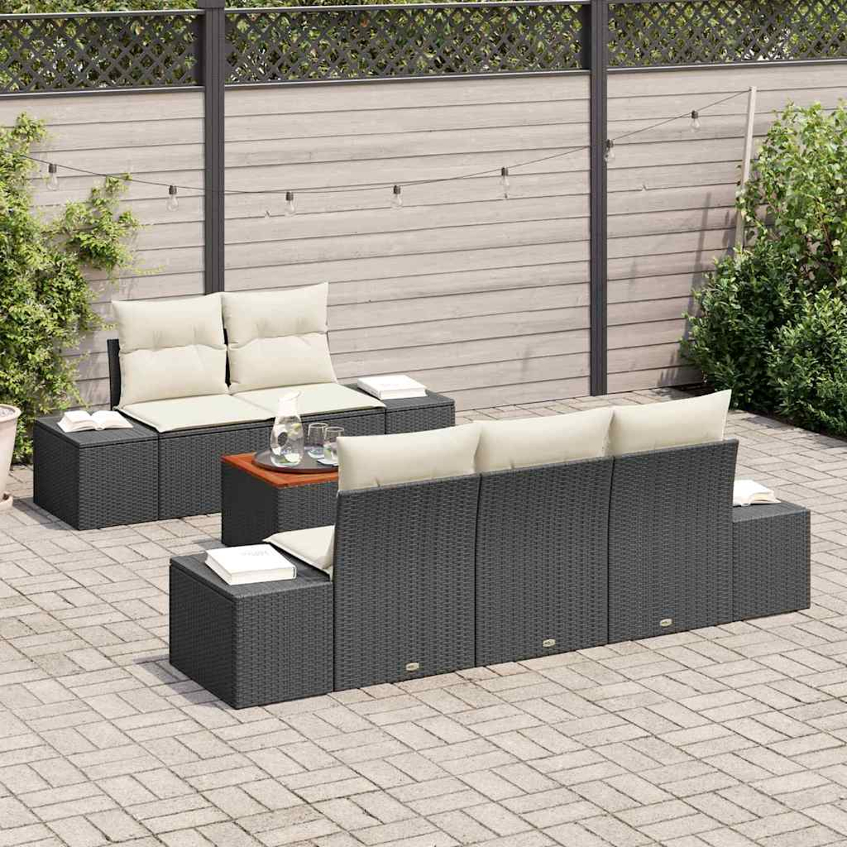 Gartenmöbel-Set mit grauem Korbgeflecht, cremefarbenen Kissen und Holztisch. Vor einem Holzzaun mit Lichterketten.