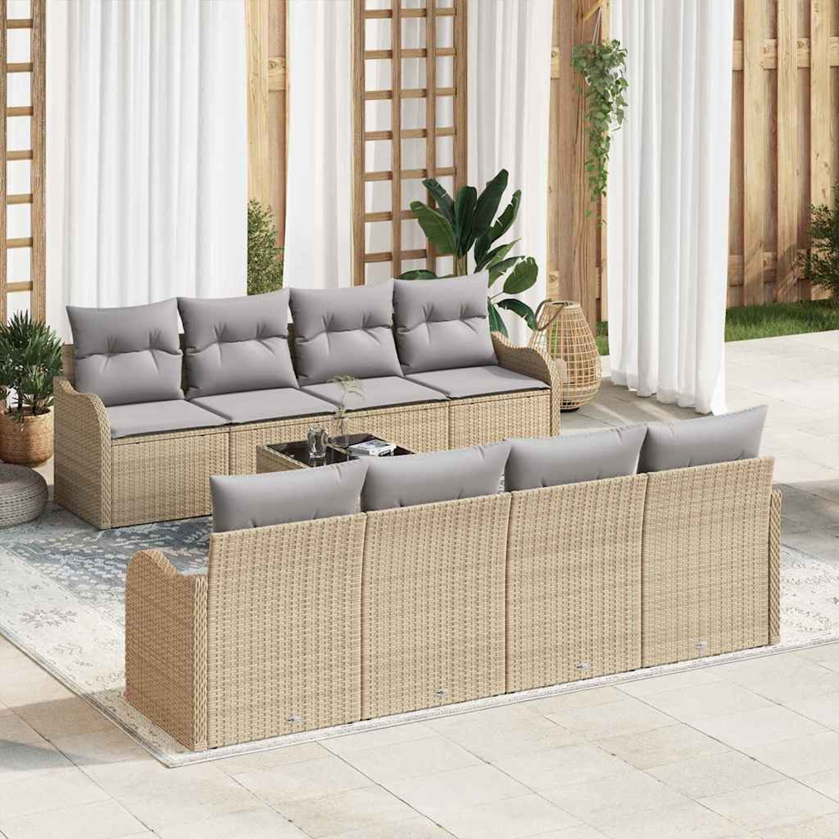 Geflochtenes Sitzset für draußen mit grauen Kissen. Enthält zwei Sofas, einen Couchtisch und Zierpflanzen. Vor durchsichtigen Vorhängen.