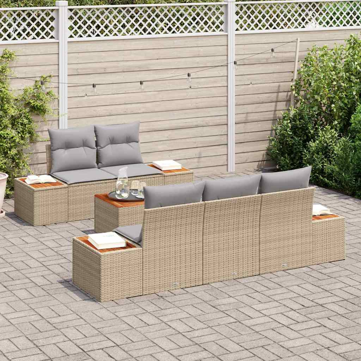 Garten-Sitzgruppe. Beige Korbsessel mit grauen Kissen auf einer Backstein-Terrasse, Holztische. Holzzaun im Hintergrund.