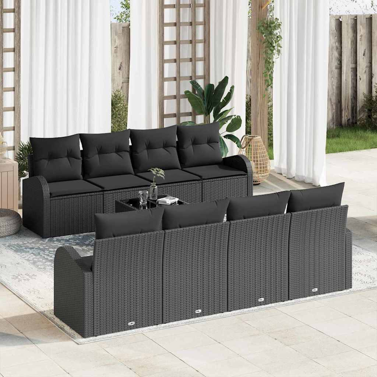 Szene im Freien mit schwarzen Korbmöbeln, darunter ein Sofa und Stühle, auf einer Terrasse. Weiße Vorhänge und Pflanzen im Hintergrund.