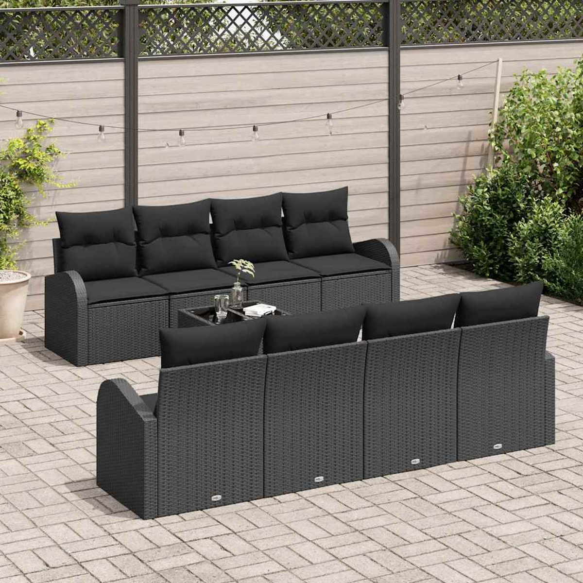 Garten-Terrassenset mit schwarzem Rattansofa, Kissen und Tisch. Holzzaun und Grün im Hintergrund.