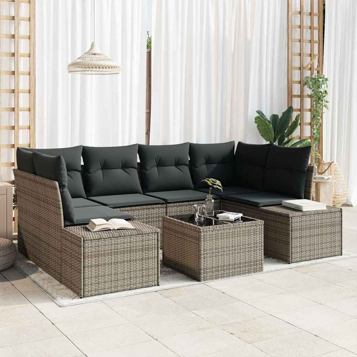 Outdoor-Rattansofa-Set mit grauen Kissen, Couchtisch, Büchern und Pflanzen. Hintergrund: weiße Vorhänge, Spalier und eine Hängepflanze.