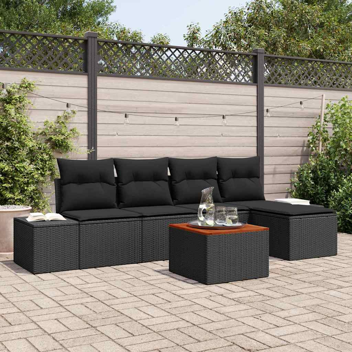 Outdoor-Set aus schwarzem Korbmöbeln mit Kissen, einem Couchtisch und einem hölzernen Zaun im Hintergrund mit Lichterketten.