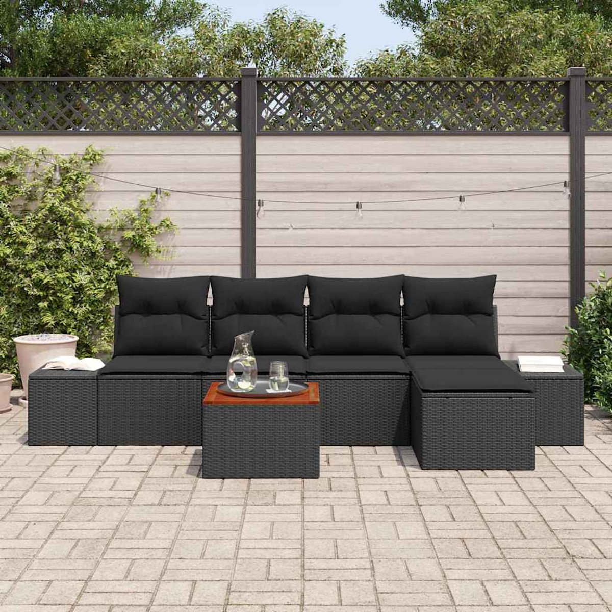 Outdoor-Sofa aus schwarzem Korbgeflecht mit schwarzen Kissen, einem Holztisch mit Glas und einem Krug in einem Hinterhof.