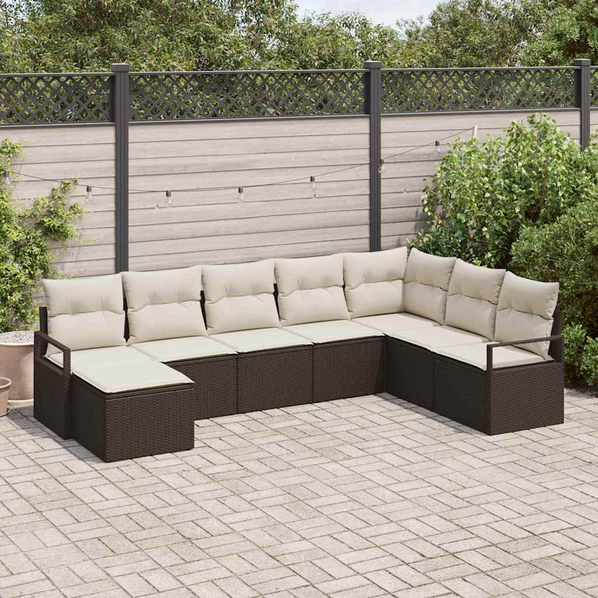 Ein L-förmiges Ecksofa mit hellen Kissen steht auf einer gepflasterten Terrasse. Ein Holzzaun und Grün bilden den Hintergrund.