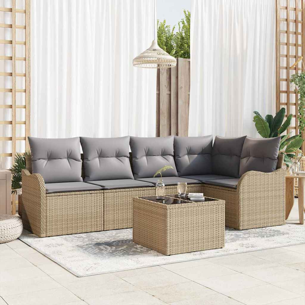 Geflochtenes Outdoor-Ecksofa mit grauen Kissen, passender Couchtisch auf einem Teppich. Weiße Vorhänge und eine Hängelampe im Hintergrund.