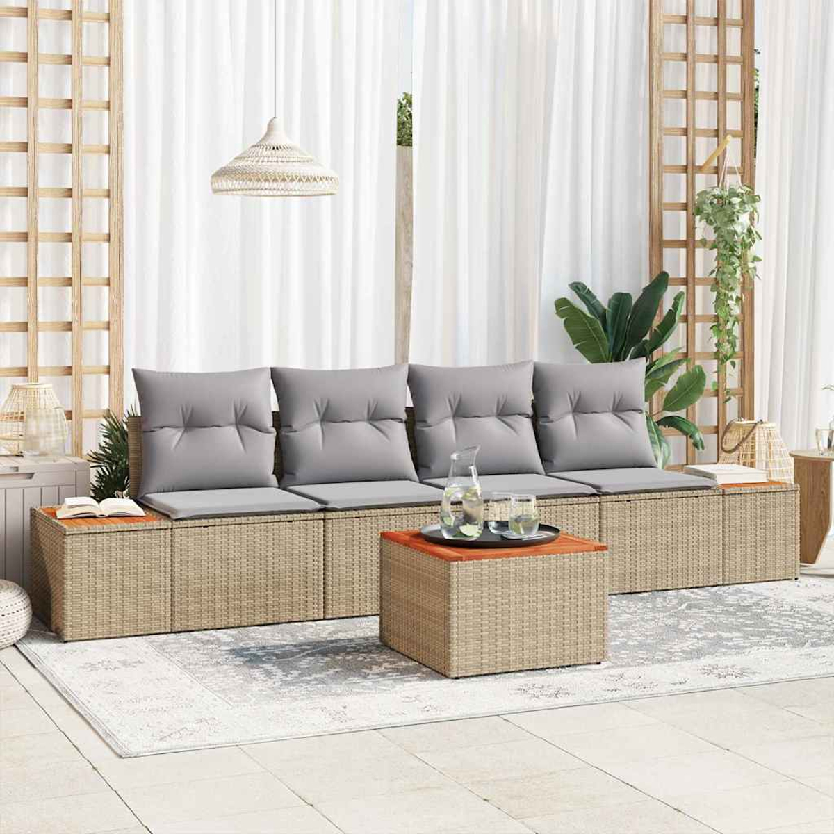 Außenbereich mit grauen Kissen, Couchtisch und Teppich. Weiße Vorhänge, Holzgitter und Hängepflanzen sind sichtbar.