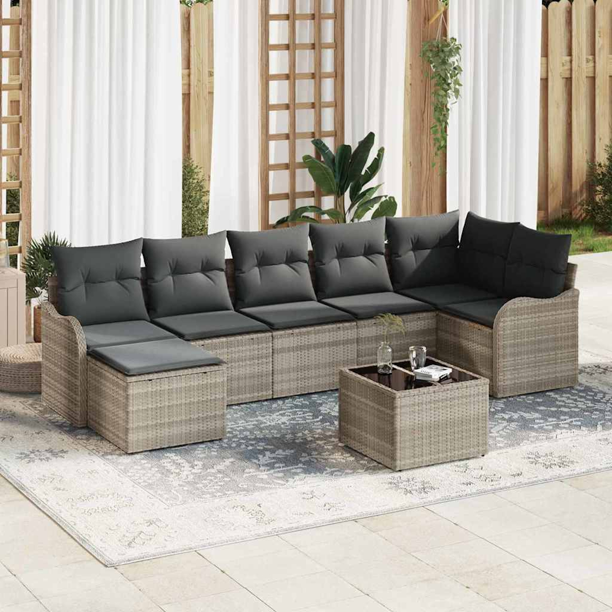 Outdoor-Rattan-Ecksofa mit grauen Kissen und einem quadratischen Couchtisch auf einem gemusterten Teppich; weiße Vorhänge im Hintergrund.