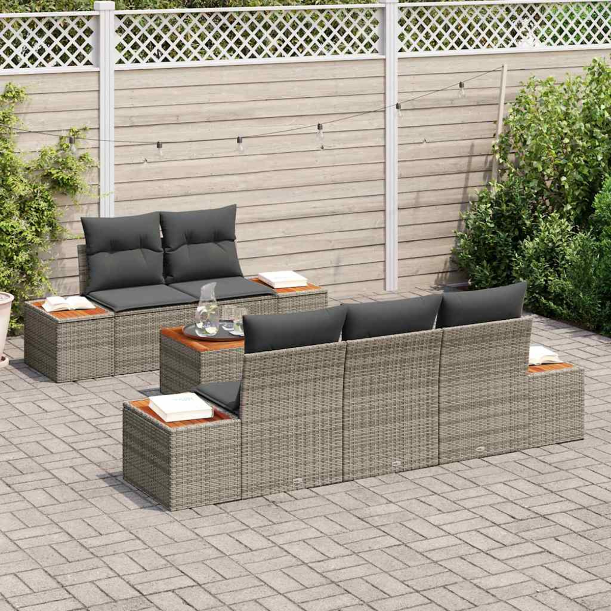 Gartenmöbel-Set. Es besteht aus grauen Sofas im Korbgeflecht-Stil mit dunkelgrauen Kissen und Holztischplatten auf einem Ziegelpflaster.