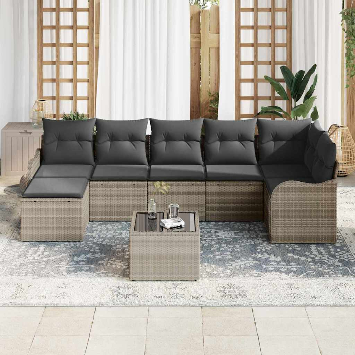 Outdoor-Ecksofa mit grauen Kissen und einem kleinen Tisch. Auf einem gemusterten Teppich mit Fenstern im Hintergrund.