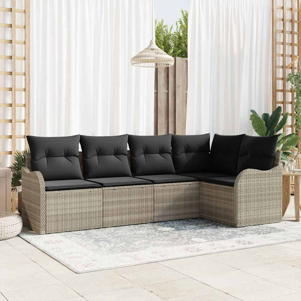 Ein Ecksofa im Freien mit dunklen Kissen. Es steht auf einem Teppich, mit weißen Vorhängen und einer gewebten Leuchte im Hintergrund.