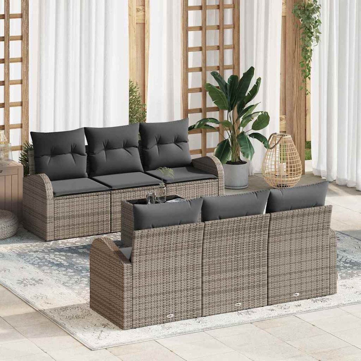 Zwei Rattansofas mit grauen Kissen stehen auf einem Teppich. Eine große Pflanze im Topf, eine Laterne und weiße Vorhänge sind im Hintergrund.