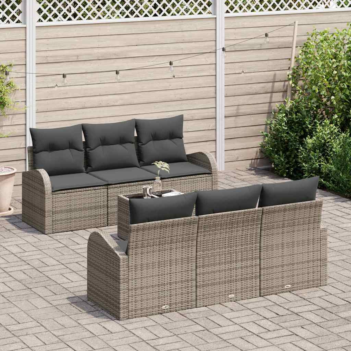 Garten-Wicker-Sofagarnitur mit grauen Kissen. Ein kleiner Tisch und ein grüner Busch befinden sich im Hintergrund.