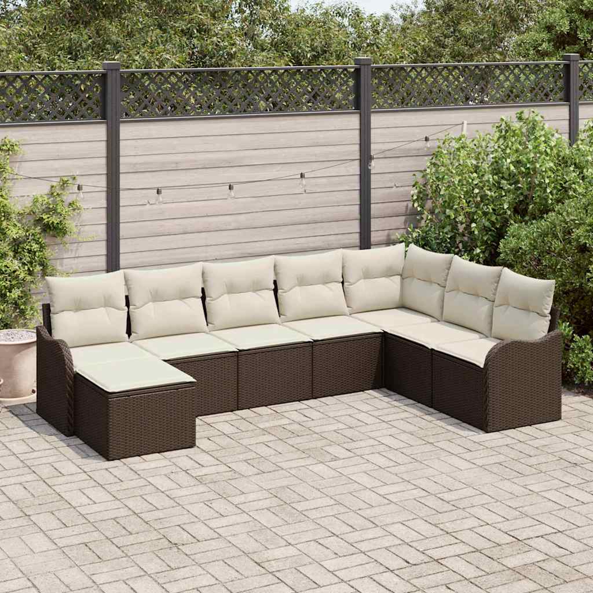 Braunes Korbsessel-Sofa mit cremefarbenen Kissen auf einer Backstein-Terrasse. Im Hintergrund sind ein Holzzaun und Grünflächen zu sehen.