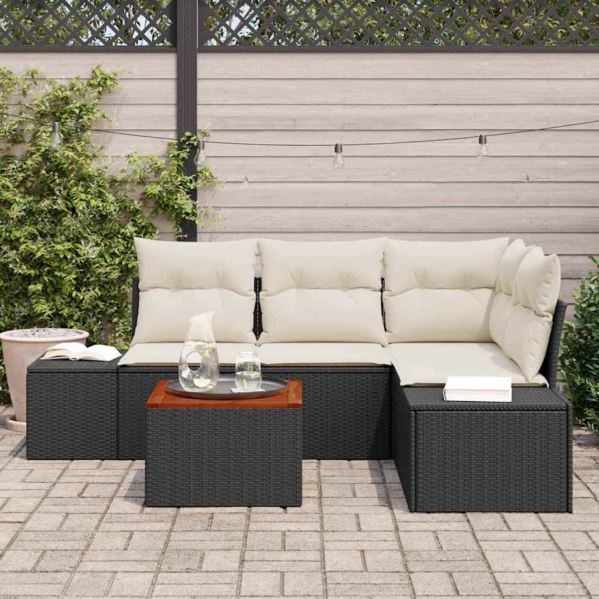 Outdoor-Ecksofa mit beigen Kissen und kleinem Tisch mit Wasserglas und Krug. Grüne Pflanzen und Holzzaun im Hintergrund.