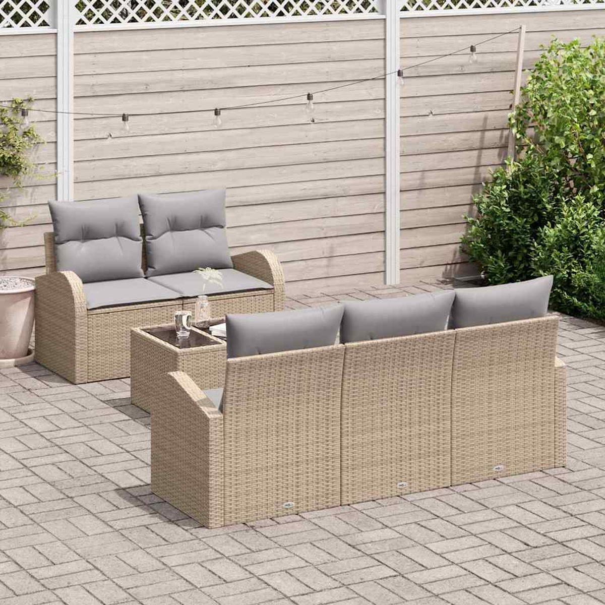 Gartenmöbel-Set aus Korb: ein Loveseat, ein Dreisitzer-Sofa und ein Tisch. Graue Kissen. Holzzaun und Lichterkette im Hintergrund.