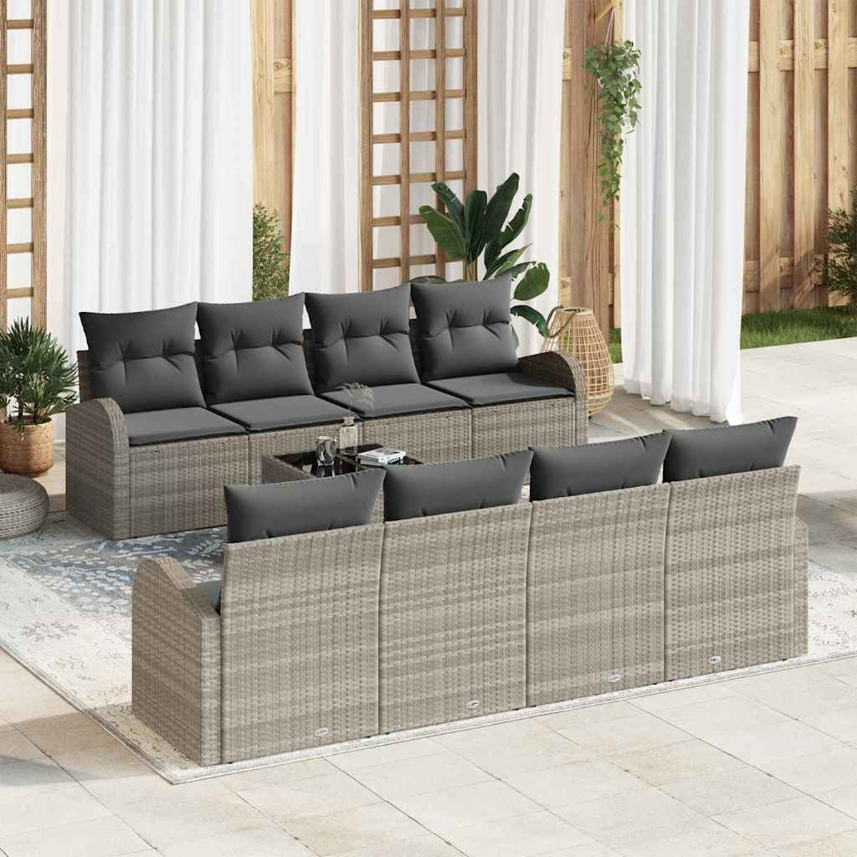 Gartenmöbel-Set. Graue Korbsessel mit dunkelgrauen Kissen. Ein Tisch mit Glasplatte steht zwischen den Sofas. Weiße Vorhänge im Hintergrund.