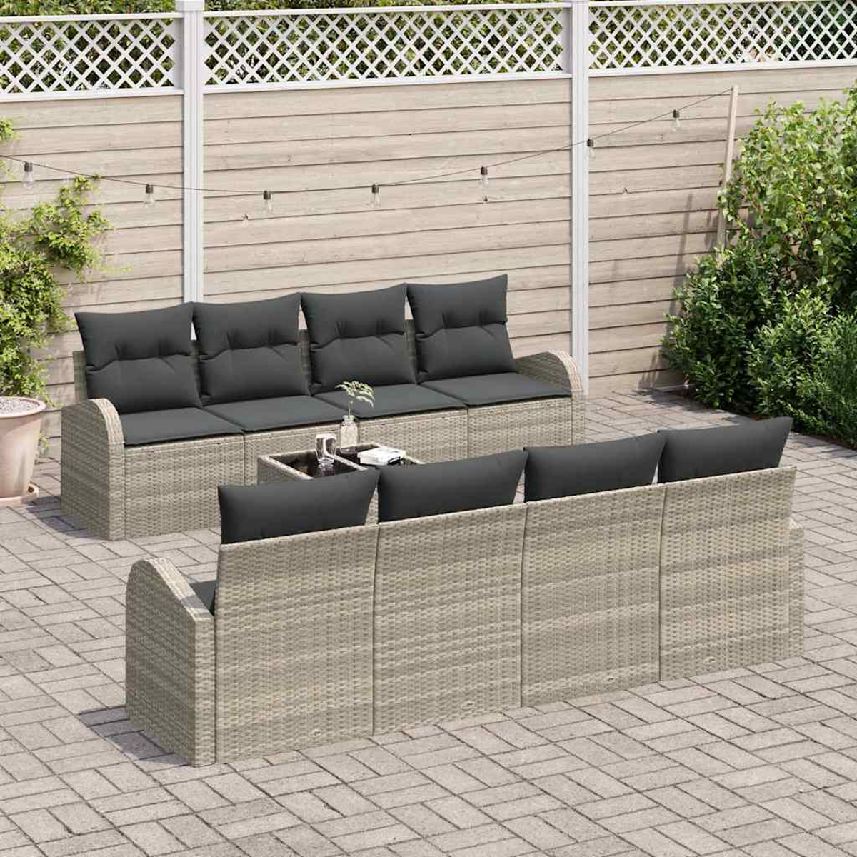 Garten-Set mit grauen Kissen auf hellen Rattanmöbeln. Vorne steht ein Tisch mit Glasplatte. Im Hintergrund sind ein Holzzaun und Grünpflanzen.