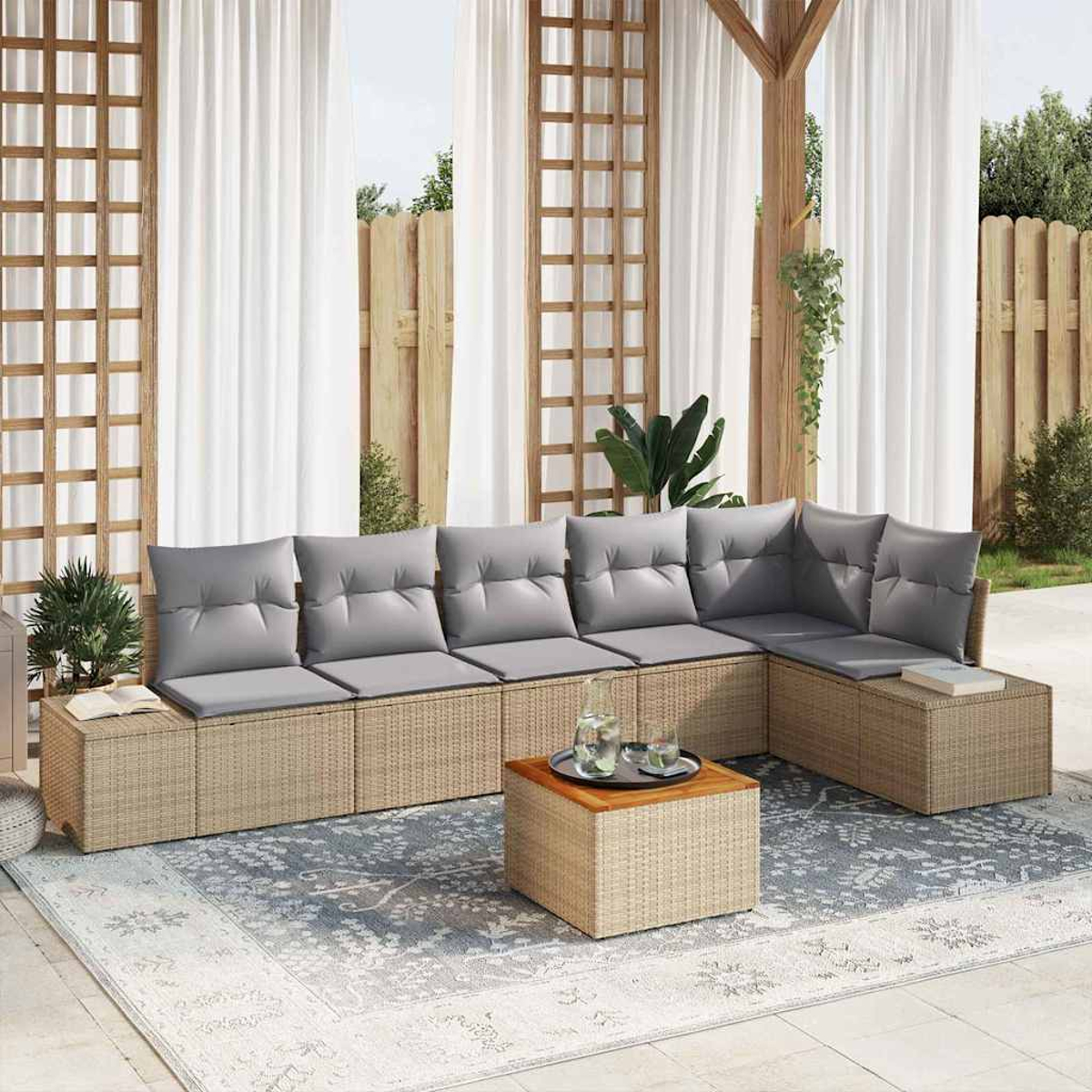 Outdoor-Sitzbereich mit grauen Kissen. Korbmöbel auf einem gemusterten Teppich. Weiße Vorhänge und Holzgitter im Hintergrund.