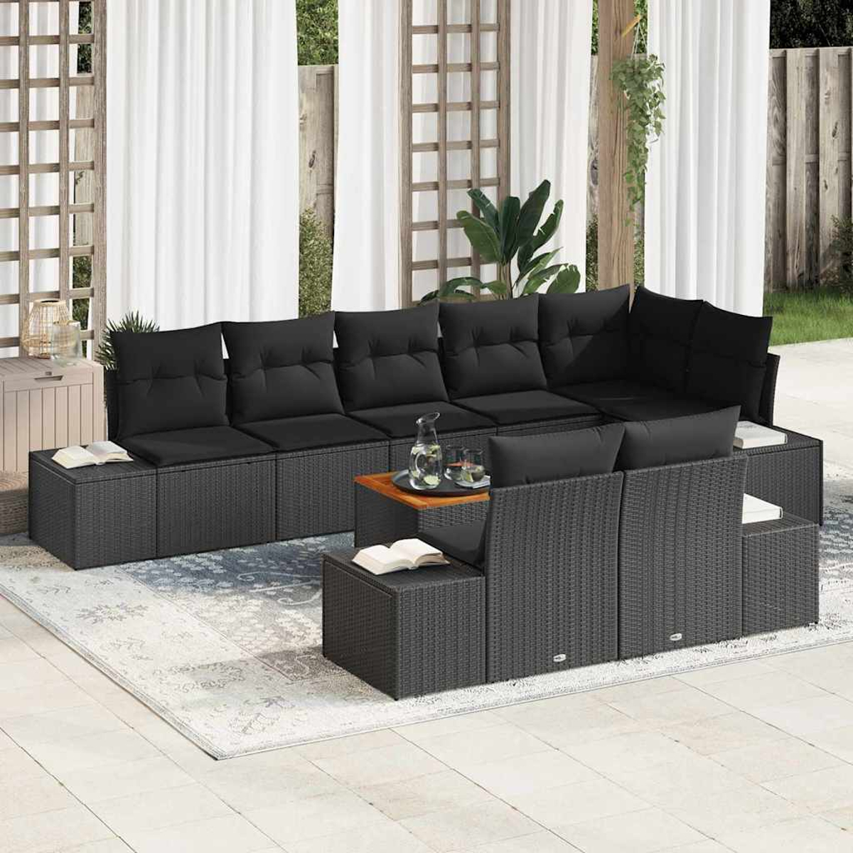 Gartensofa mit schwarzen Kissen, Couchtisch und Teppich. Im Hintergrund weiße Vorhänge und Holzgitter.