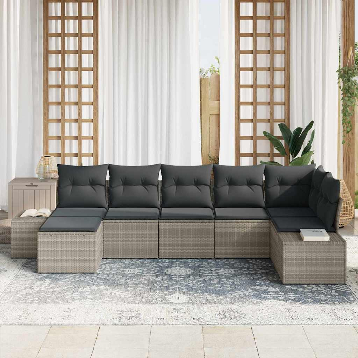 Outdoor-Ecksofa mit dunkelgrauen Kissen auf einem gemusterten Teppich. Weiße Vorhänge, Holzgitter und Pflanzen im Hintergrund.