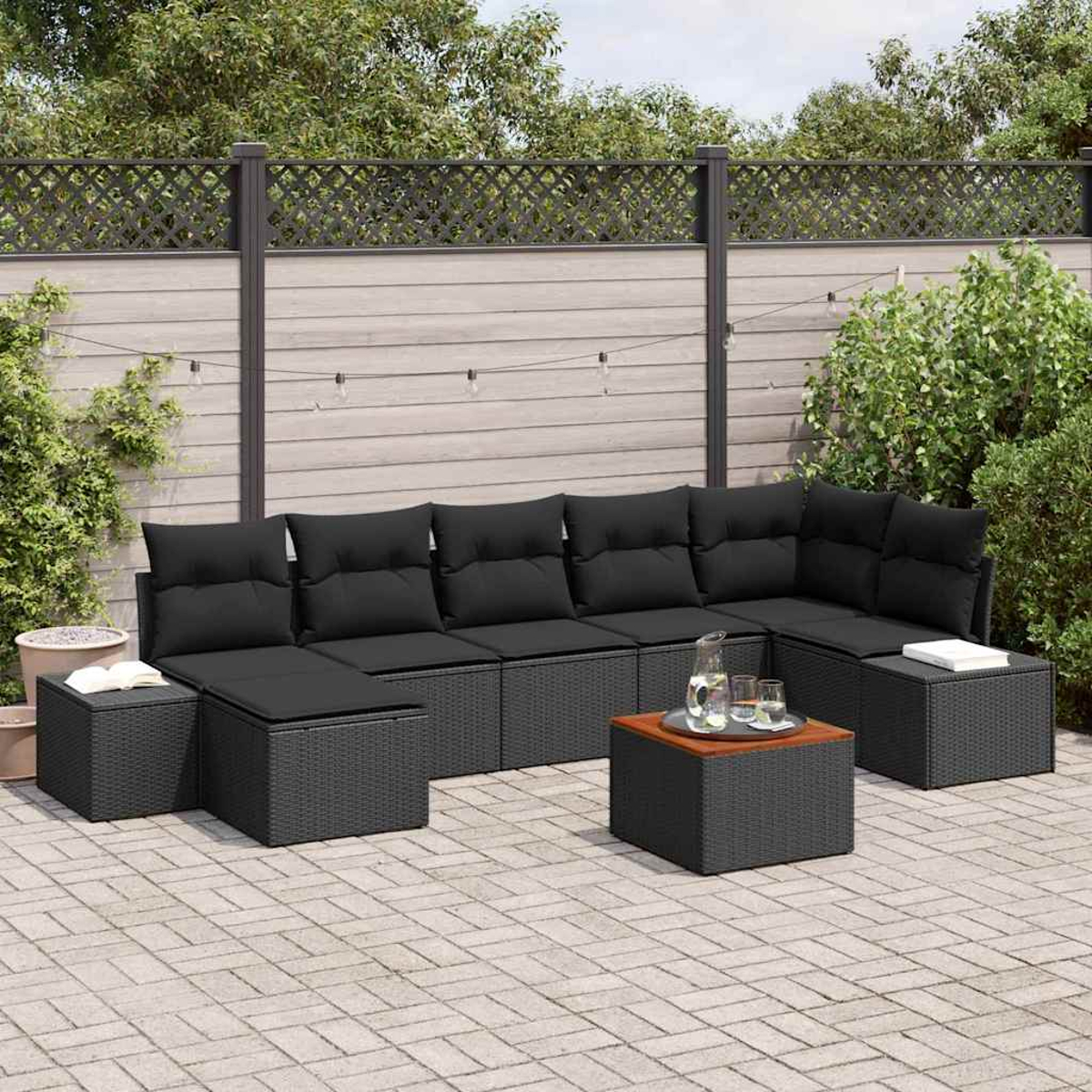 Sofá seccional al aire libre con cojines negros y mesa de madera en patio. Fondo con valla y vegetación.